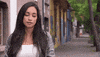 Reality TV gif. Victoria Fuller on The Bachelor shrugs with an uncertain half smile as she stands on a tree-lined sidewalk.
