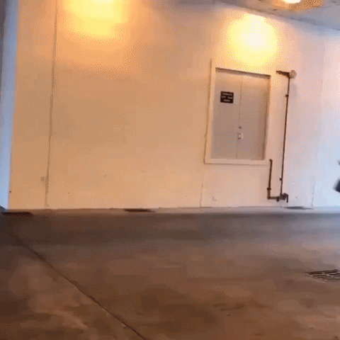 Video gif. A man runs at top speed through a parking garage and out into the daylight.