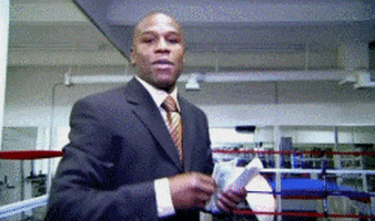 Sports gif. Floyd Mayweather is wearing a suit and is standing in a ring while tossing money at us. He looks very cocky and he throws one bill at at time.