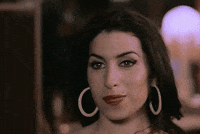 Music video gif. Amy Winehouse in her video for In My Bed, with a shy smile, waves at us flirtatiously.