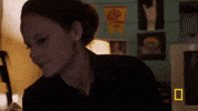 Video gif. A woman leans over a man who is lying in bed and gives his a long, tender kiss on the forehead.