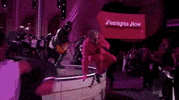 Oscars 2024 GIF. Ryan Gosling, dressed in a Barbie pink tuxedo and sunglasses, hops off the stage and rolls punches at us dramatically.