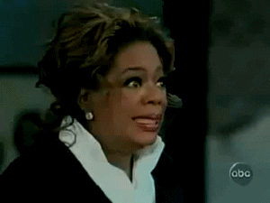 TV gif. Oprah Winfrey stares straight ahead with wide eyes and a forced smile through gritted teeth. Her eyes quickly flash to one side before looking back like she's extremely uncomfortable with what's happening. 