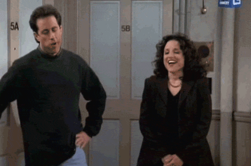 Seinfeld gif. Julia Louis Dreyfus as Elaine pumps her fist excitedly while Jerry stands to the side with his hand on his hip, appearing annoyed.