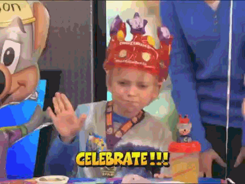 Mladý chlapec s korunou z papíru, tancující u narozeninového dortu s nápisem "Celebrate!". 