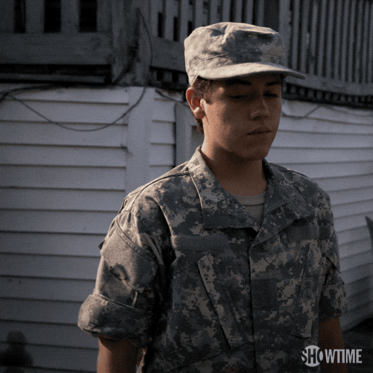 TV gif. Ethan Cutkosky as Carl in Shameless wears a military uniform and cap and he salutes us while standing in his backyard.