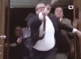 TV gif. Drew Carey in The Drew Carey Show leads a crowd out of a building and into the street, creating a big celebration of running people.