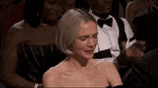 Oscars 2024 GIF. Grateful, Cary Mulligan scrunches up her face and puts a hand to her heart while the crowd applauds her. 