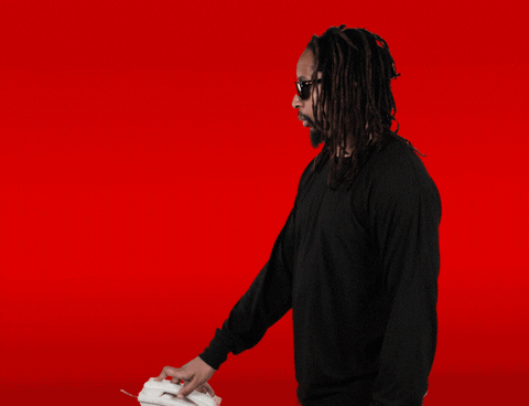Celebrity gif. Against a red background, Lil Jon picks up a corded landline phone, holding it to his ear before turning to us with a big smile and saying, "What?" which appears as text in large white bubble letters.