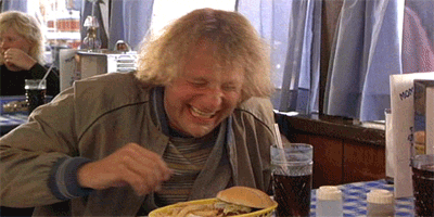 Movie gif. Jeff Daniels as Harry Dunne in Dumb and Dumber sits in a restaurant booth with a burger and soda in front of him. He laughs and flaps his hands up and down in excitement, and then hides his face in his hand.