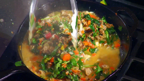 TV gif. From MasterChef, a set of silver tongs gently stir a saucepan bubbling with a hot stew filled with vegetables.