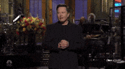 SNL gif. Elon Musk as host turns his palms out in a shrug as he rolls his eyes with a bewildered expression.
