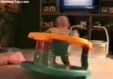 Video gif. A baby in a stationary rocker seat spinning around rapidly.