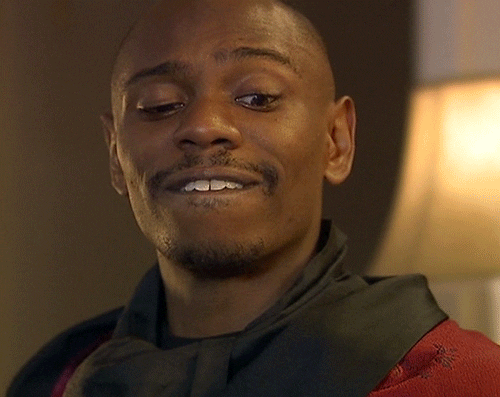 TV gif. Dave Chappelle in the Love Contract Chappelle Show skit wears a red smoking jacket, bites his lip, lowers his eyes, looking around, as he raises one eyebrow in thought.