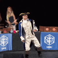 Video gif. A man in colonial era breeches, jacket, and tricorn hat strikes a lunging pose on stage and emphatically points in the air. Text, "This."