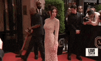 Met Gala 2024 gif. Emily Ratajkowski wearing a sandy sheer Versace gown, poses shoulder first, then shifts, posing square with arm across her torso.