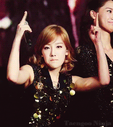 Celebrity gif. Taeyeon looks at us sternly while giving us the finger with both hands, holding a mic in one hand.