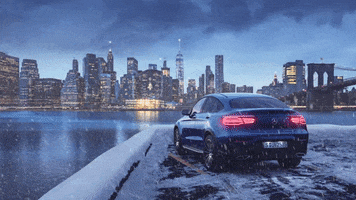 Photo gif. Snow falls on a navy Mercedes sedan parked beneath the Brooklyn Bridge across the East River from the lights of the New York City skyline.