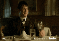 TV gif. Robin Lord Taylor as Oswald Cobblepot in Gotham smiles and raises his glass to cheers.