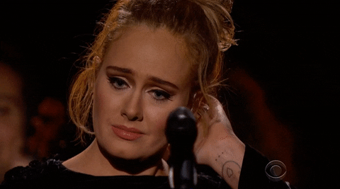 Celebrity gif. Adele stands on stage in front of a microphone. She rubs the back of her neck with teary eyes and then says, “Thank you” to the crowd in front of her.