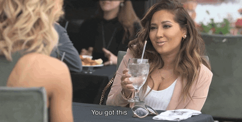 Reality TV gif. Adrienne Bailon on Sisterhood of Hip Hop. She's sitting at an outdoor table with a friend and holds a drink up as she encourages a friend, saying, "You got this."