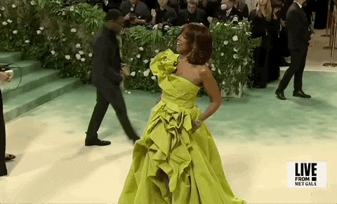 Met Gala 2024 gif. Gayle King posing for the cameras, in a chartreuse gown with big, bunched draping details, as she hams for the cameras, then relaxes into a more natural smile.