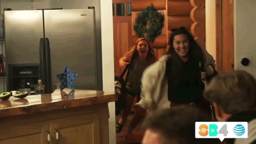 Reality TV gif. From Summer Break, an excited Zoe runs into a kitchen and hugs Ben as Kaylee runs up behind them and jumps into their hug.