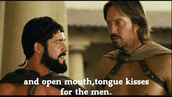 Movie gif. Sean Maguire as Leonidas and Kevin Sorbo as Captain in Meet the Spartans smile and nod at each other awkwardly. Text, "And open mouth, tongue kisses for the men."