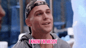 Reality TV gif. Man from Ex on the Beach wearing a camo backwards baseball cap smiles and glances over and says, "I know I'm messy," which appears as text.