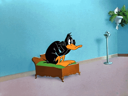 Cartoon gif. A worried Daffy Duck sits on a tiny bed, gently slapping his cheeks.