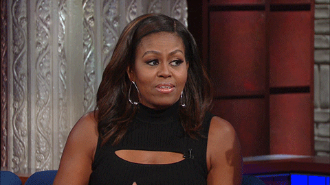 Political gif. Michelle Obama sits in a chair on the set of The Late Show with Stephen Colbert. She sighs and tips her head like, "What can you do."
