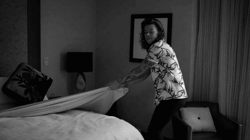 Celebrity gif. Harry Styles is pulling the sheets off of a hotel bed, the video transitioning to slow motion when the blanket flies in the air.