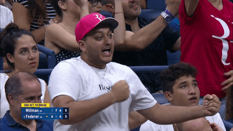 Sports gif. A man stands up from bleachers at a crowded sports game. He beats his chest and balls up his fist. He looks super hyped up and yells, “lets goooo.”
