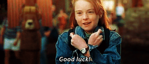 Movie gif. Lindsay Lohan as Hallie in The Parent Trap. She has both arms crossed over her chest and both her fingers are crossed as well. She says, "Good luck," and smiles.