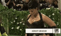 Met Gala 2024 gif. Snap-zoom out and back in on Ashley Graham posing for all angles, wearing a custom Ludovic de Saint Sernin gown with black leather bodice and sheer beaded skirt.