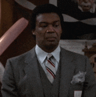 Video gif. Man wearing a suit with a pocket square clenches his jaw and closes his eyes as he shakes his head almost imperceptibly.