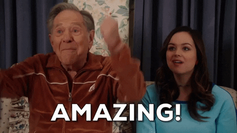 TV gif. Sitting next to Hayley Orrantia as Erica, George Segal as Pops on The Goldbergs raises his fists in excitement and says, “Amazing!”