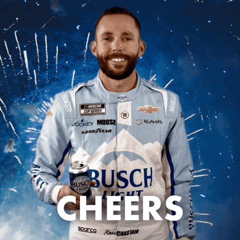 Sponsored gif. NASCAR driver Ross Chastain offers a can of Busch Light beer while fireworks explode behind him. He wears a driver fire suit decorated with many sponsor logos with the largest being the Busch Light beer logo across the center of his abdomen. Text reads, “Cheers.”