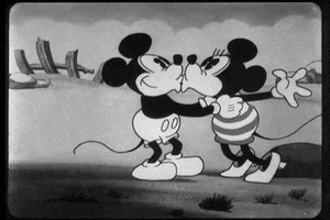 Disney gif. In a black-and-white scene, Minnie and Mickey Mouse kiss twice and then embrace.