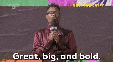Video gif. A man in black glasses and a lustrous maroon shirt, clutches a microphone in his hands and speaks into it with energy. Text, "Great, big, and bold."