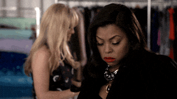 Celebrity gif. Taraji P Henson looks down, closing her eyes, and draws a cross on the top half of her body with her hand and cell phone. She looks up with an annoyed expression on her face and walks away from a woman behind her.
