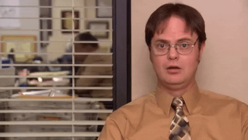 The Office gif. Rainn Wilson as Dwight looks concerned before he breaks into a laugh and brushes at the air with his hand.