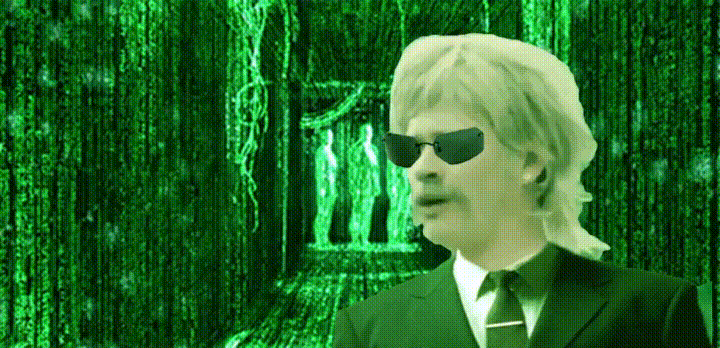 Celebrity gif. Tom Delonge from Blink-182 has a mullet, sunglasses, and is dressed in a suit. He's edited to be in front of the Matrix green screen, and he looks around confusedly while mouthing, "What the f-?!"