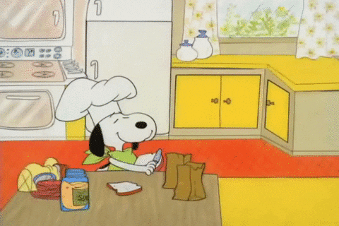 Peanuts gif. Wearing a chef's hat, a cheerful Snoopy spreads mayonnaise on a piece of bread. He tosses a slice of lunch meat over his head and catches it on the bread, topping it with another piece of bread. He repeats this process as Sally and Charlie Brown enter the scene. Snoopy bags the sandwiches and gives them to the children.