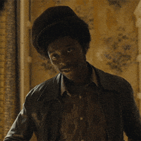 TV gif. A cast member from Small Axe has a paper boy cap on and wears a leather jacket and a vintage shirt. He grins and nods slowly and confidently.