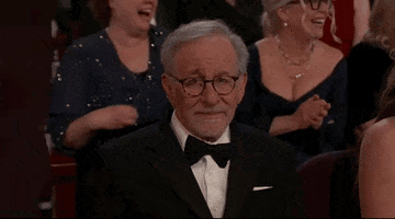 Oscars 2024 GIF. Steven Spielberg exhales a breath while shaking his head. His brows are furrowed and worry is fully plastered all over his face.