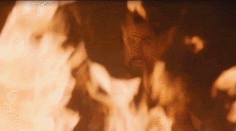 Game of Thrones gif. Emilia Clarke as Daenerys Targaryen pushes a flaming pyre to the ground in front of Joe Naufahu as Khal Moro in a room engulfed in flames.