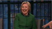 Political gif. Hillary Clinton leans forward as her mouth gapes open in laughter before she settles back in her chair.