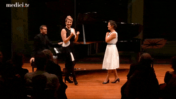 Celebrity gif. Joyce Didonato gives two triumphant raised fists as she approaches a smiling woman in front of an audience. 
