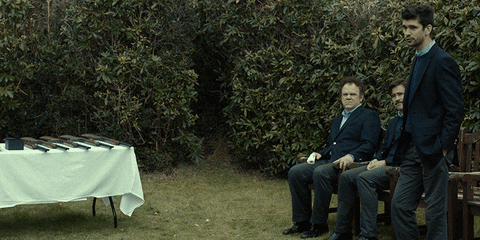 Movie gif. Colin Farrell as David and John C Reilly as the Lisping Man in The Lobster sit next to each other outside. The Lisping Man then shoves Ben Whishaw as The Limping Man. The Limping man fights back as David jumps up from his seat to stop the fight. A young waiter in the background stands still, watching.